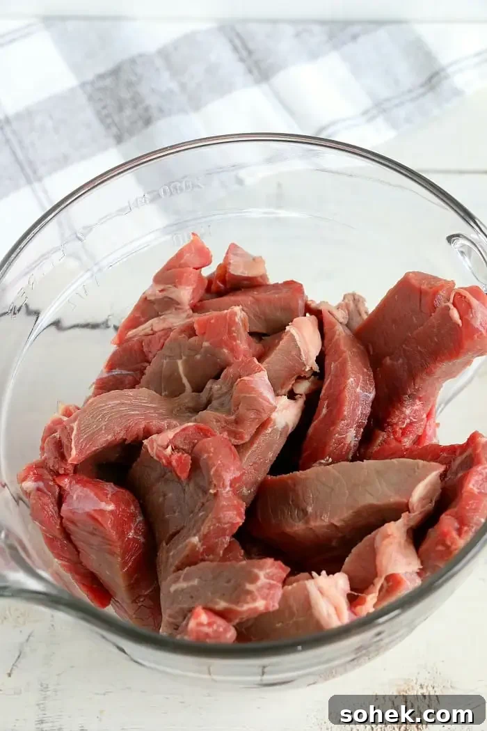 Crispy Air Fryer Beef Jerky Recipe for Homemade Snacks 9 A clear glass bowl filled with raw, thinly sliced beef pieces, perfect for making air fryer beef jerky.