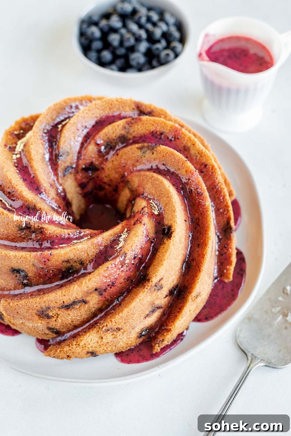Angled image of super easy blueberry bundt cake with blueberry glaze drizzled over the top | All Images © Beyond the Butter, LLC