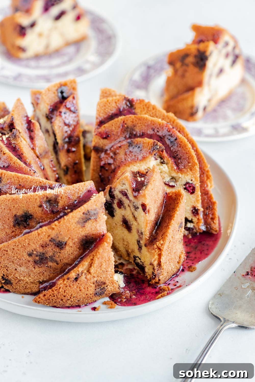 Angled image of sliced blueberry bundt cake with blueberry glaze drizzled over the top | All Images © Beyond the Butter, LLC