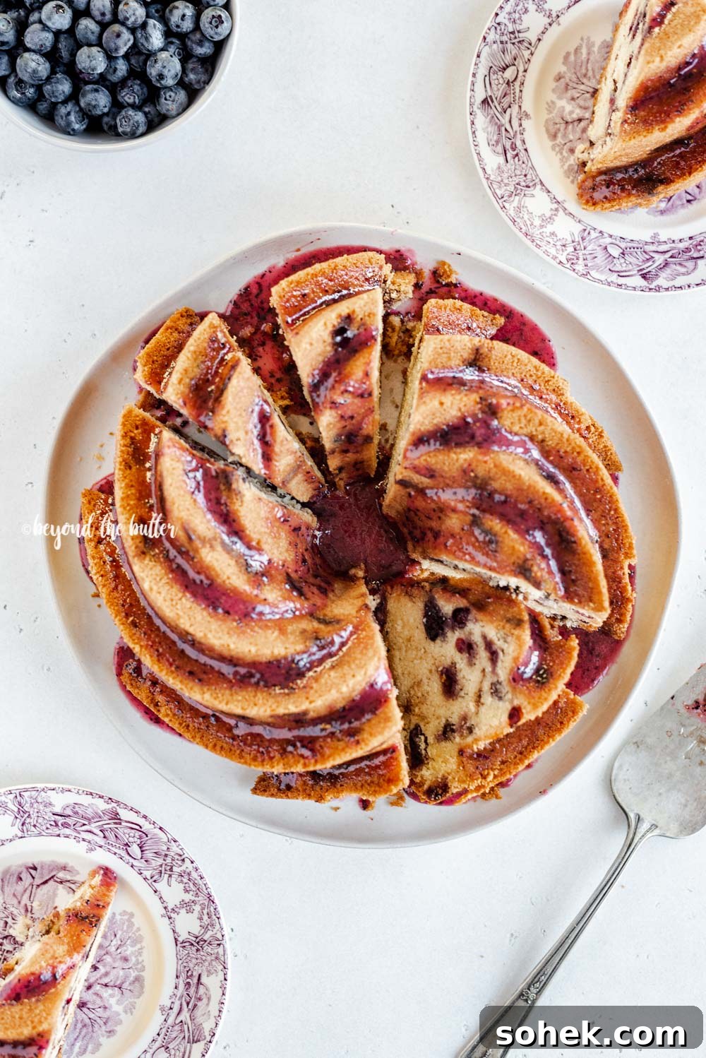 Overhead image of sliced blueberry bundt cake with blueberry glaze drizzled over the top | All Images © Beyond the Butter, LLC