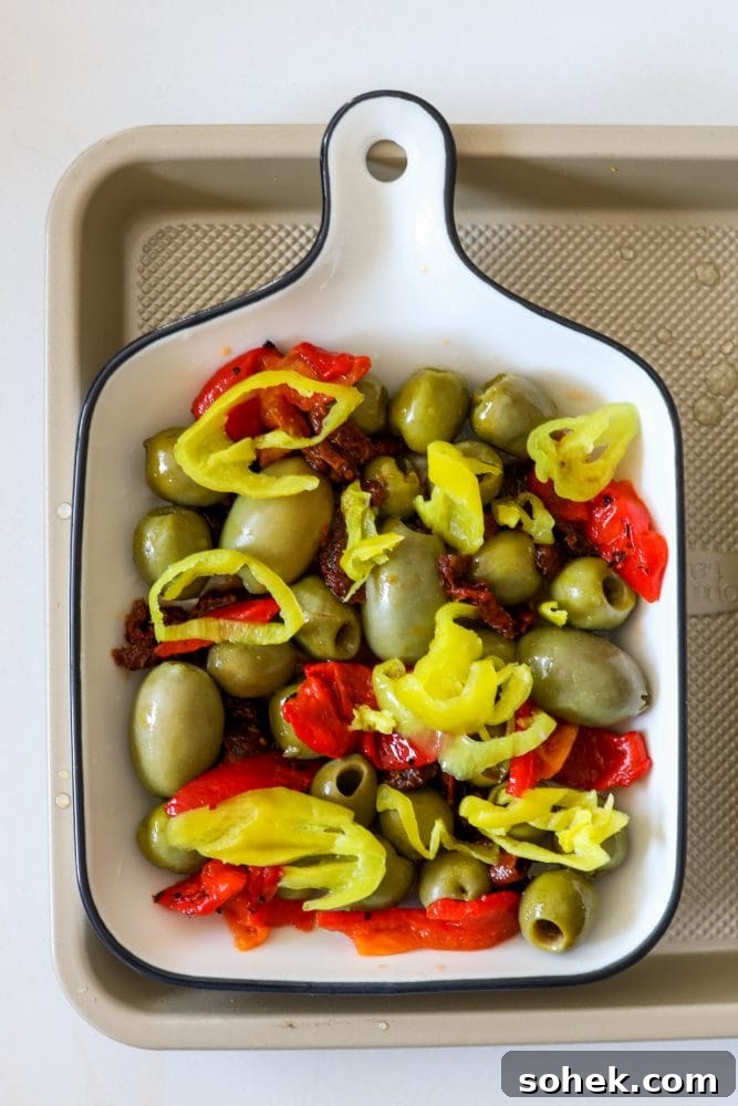 Mediterranean Baked Olives with Feta and Herbs 8 picture of olives sundried tomatoes red pepper strips and pepperoncini peppers in a baking dish