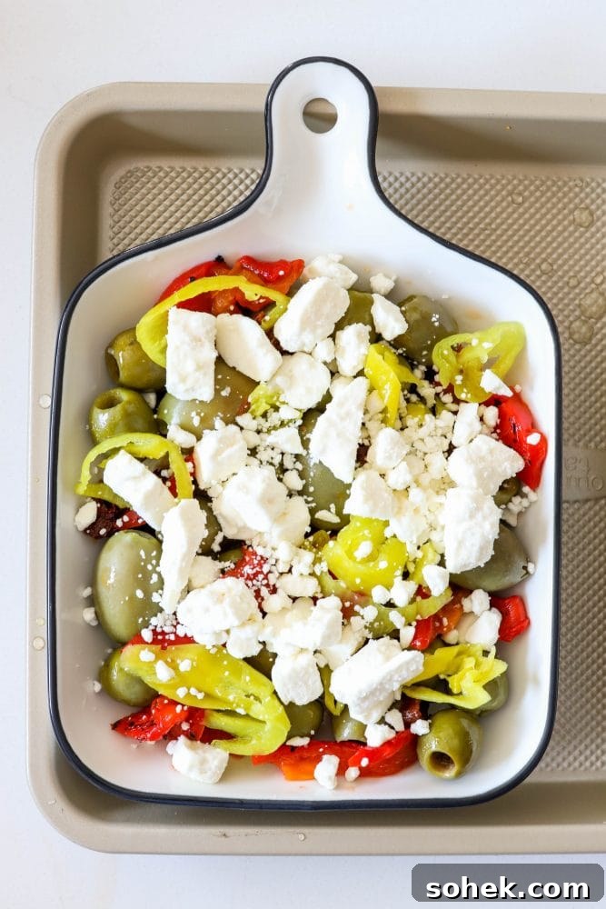 Mediterranean Baked Olives with Feta and Herbs 9 picture of olives sundried tomatoes red pepper strips and pepperoncini peppers in a baking dish with feta