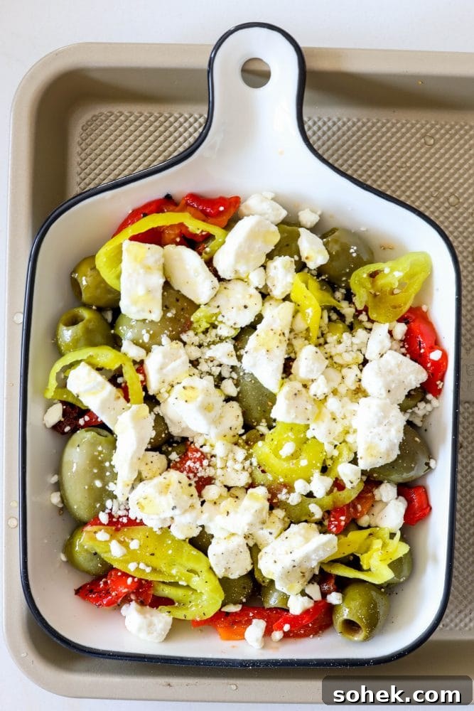 Mediterranean Baked Olives with Feta and Herbs 10 picture of olives sundried tomatoes red pepper strips and pepperoncini peppers in a baking dish with feta and herbs
