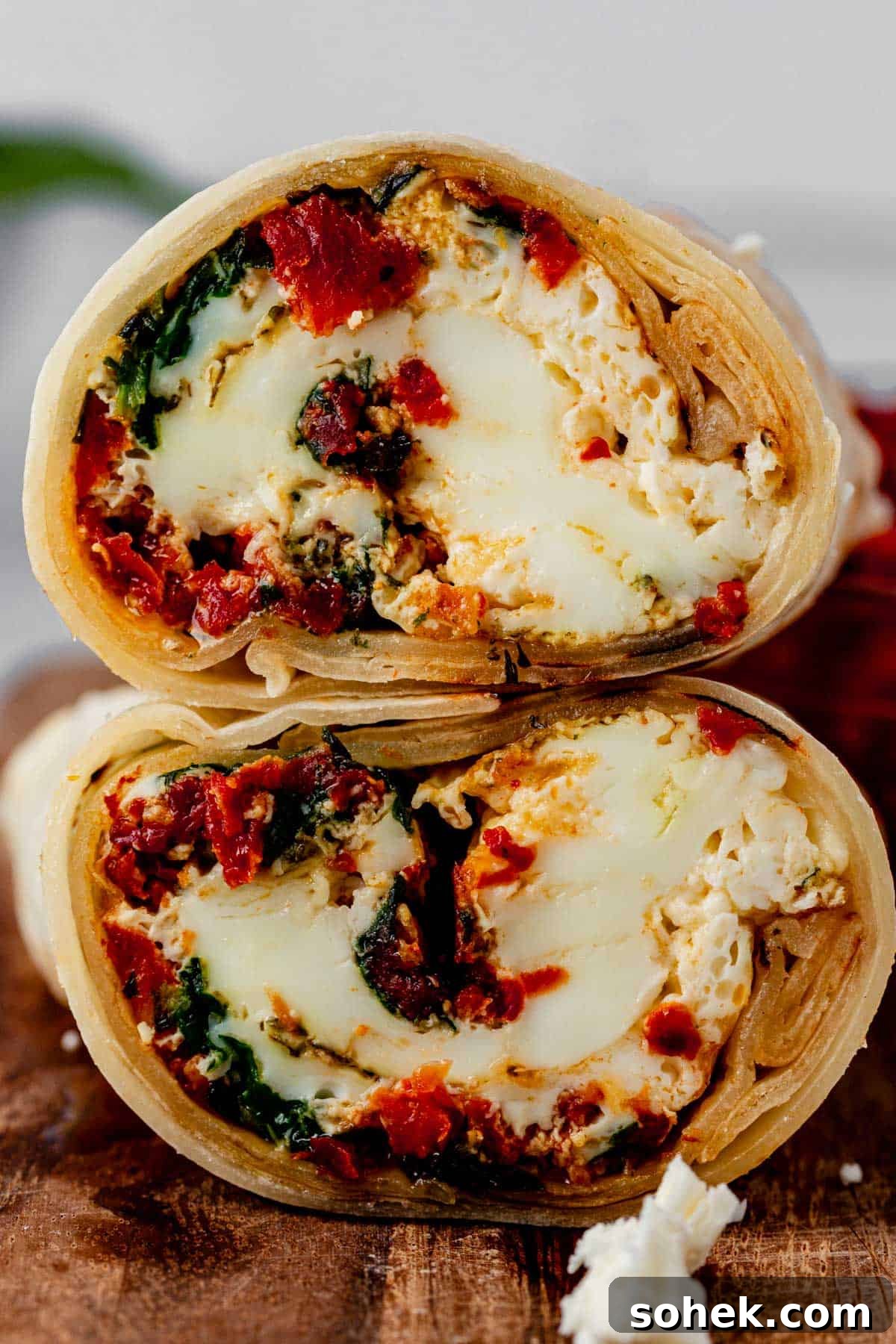 Spinach and Feta Egg White Wrap Recipe for Protein-Packed Breakfast 2 spinach feta egg white wrap cut in half and stacked on a cutting board.