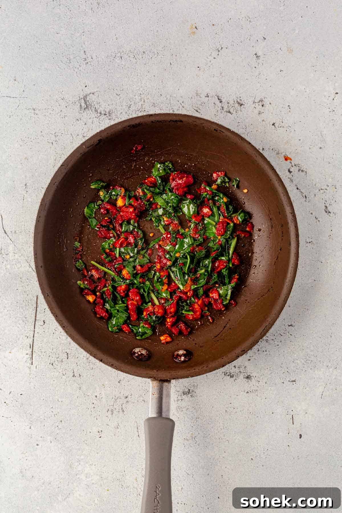 Spinach and Feta Egg White Wrap Recipe for Protein-Packed Breakfast 4 satueed spinach and sun dried tomatoes in a skillet.