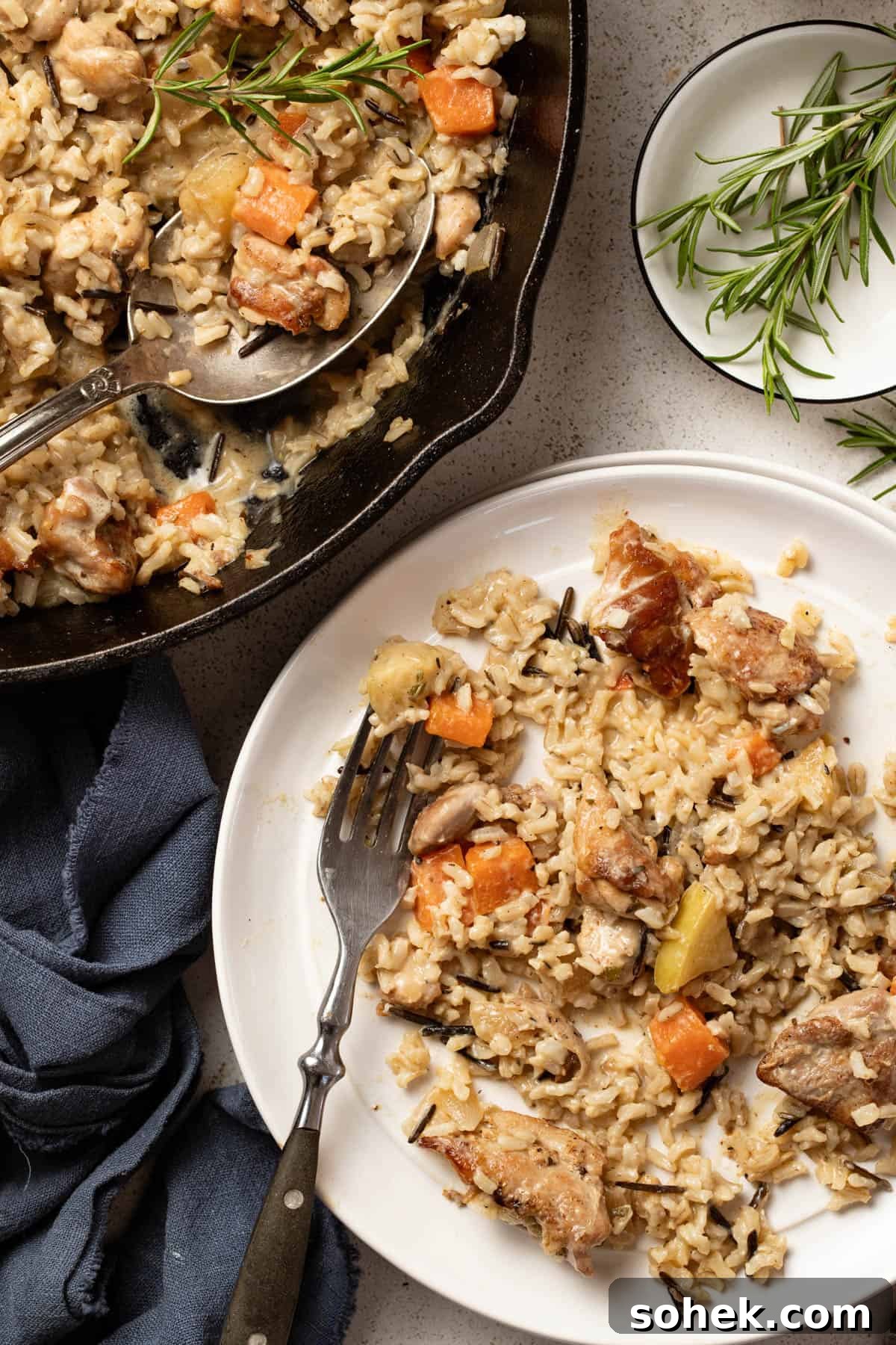 Dijon Chicken Skillet with Wild Rice and Veggies 10 Chicken and rice scooped onto a white plate next to fresh rosemary sprigs and a glass of water.