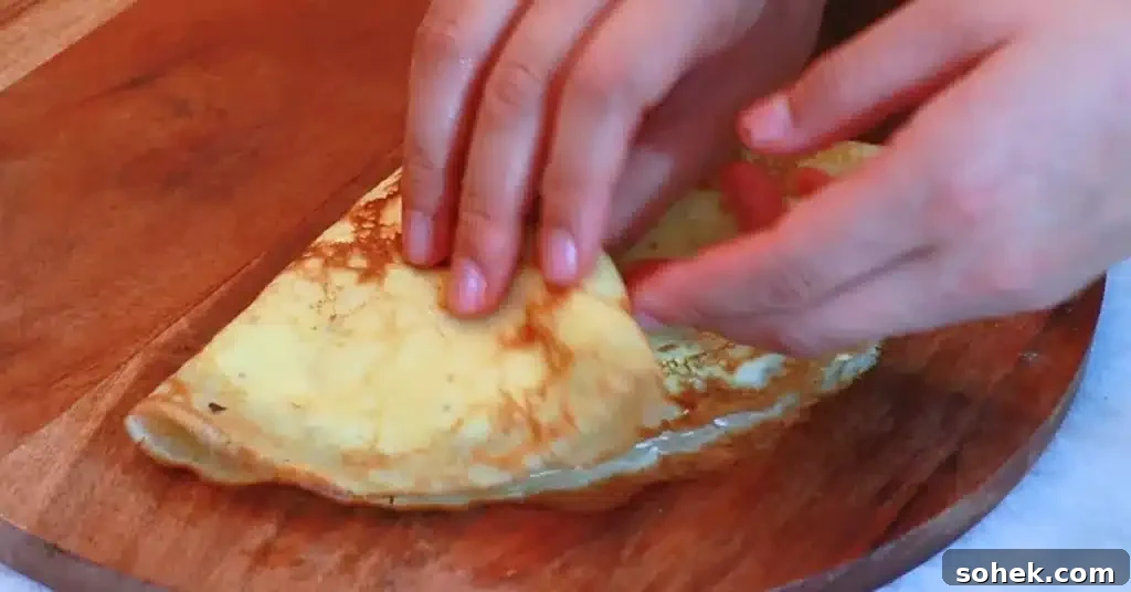 Classic French Crepes: Thin Pancake Recipe & Serving Ideas 18 folding a crepe filled with whipped cream and strawberries
