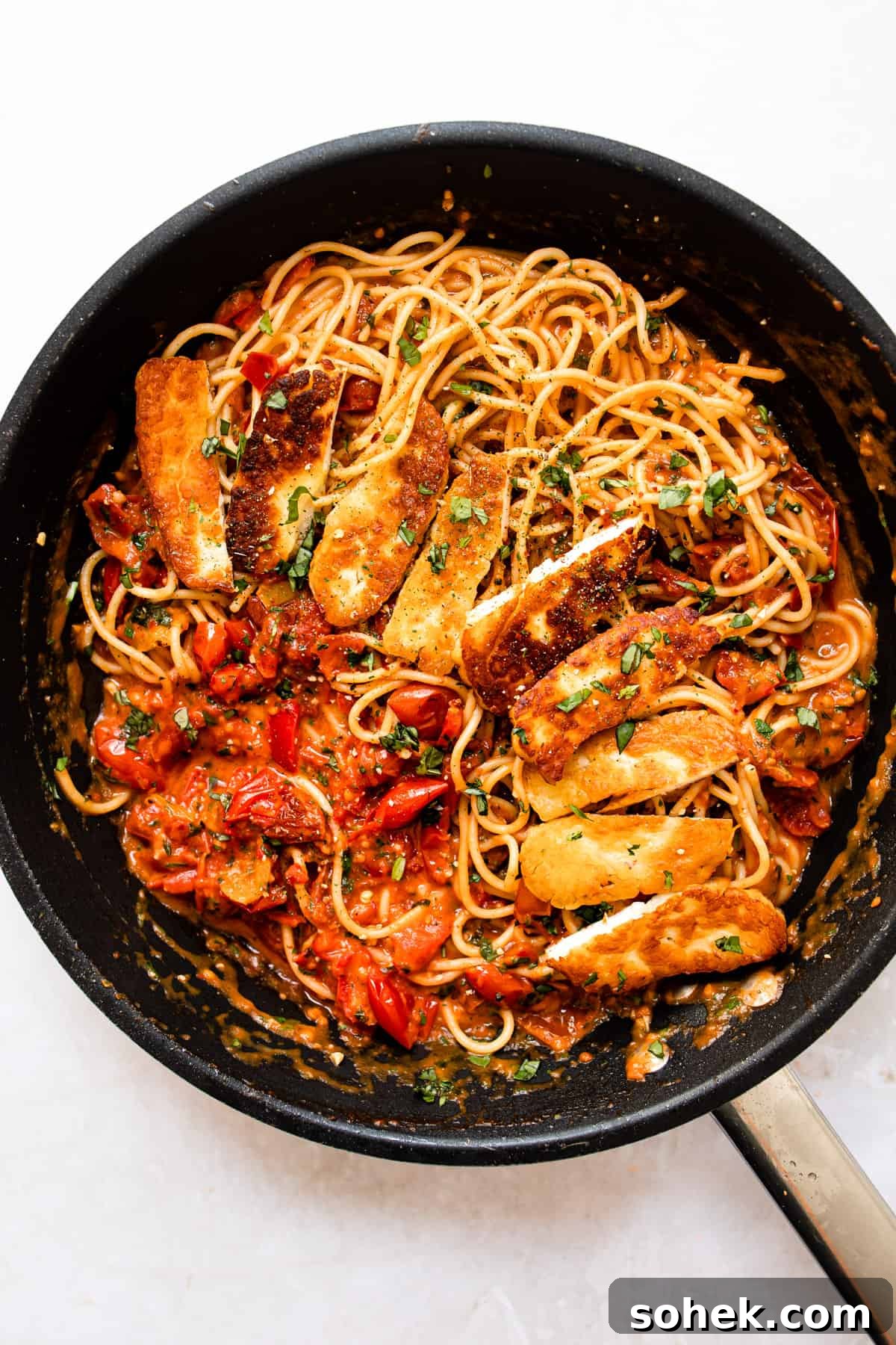 Halloumi pasta in a pan with a rich tomato sauce and fresh herbs.