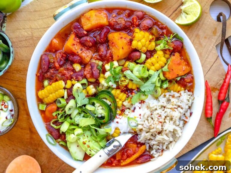 Hearty Sweet Potato Chili with Black Beans and Chipotle 18 sweet potato chili in a bowl on rice and topped with jalapeños, cilantro, lime, sour cream, avocado, and corn.