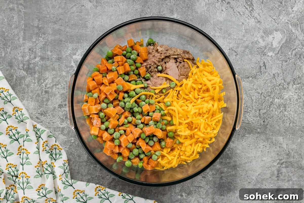 frozen peas and carrots with shredded cheese and tuna in a bowl