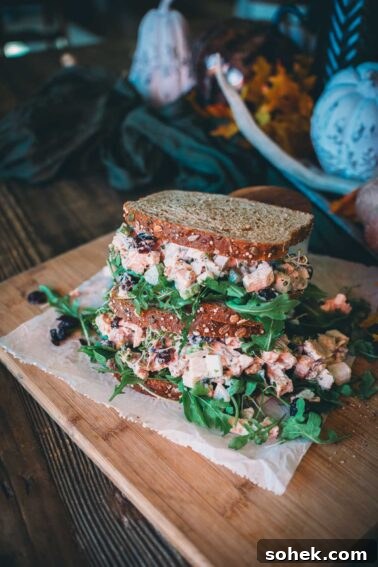 A stacked turkey salad sandwich with wheat bread and greens.
