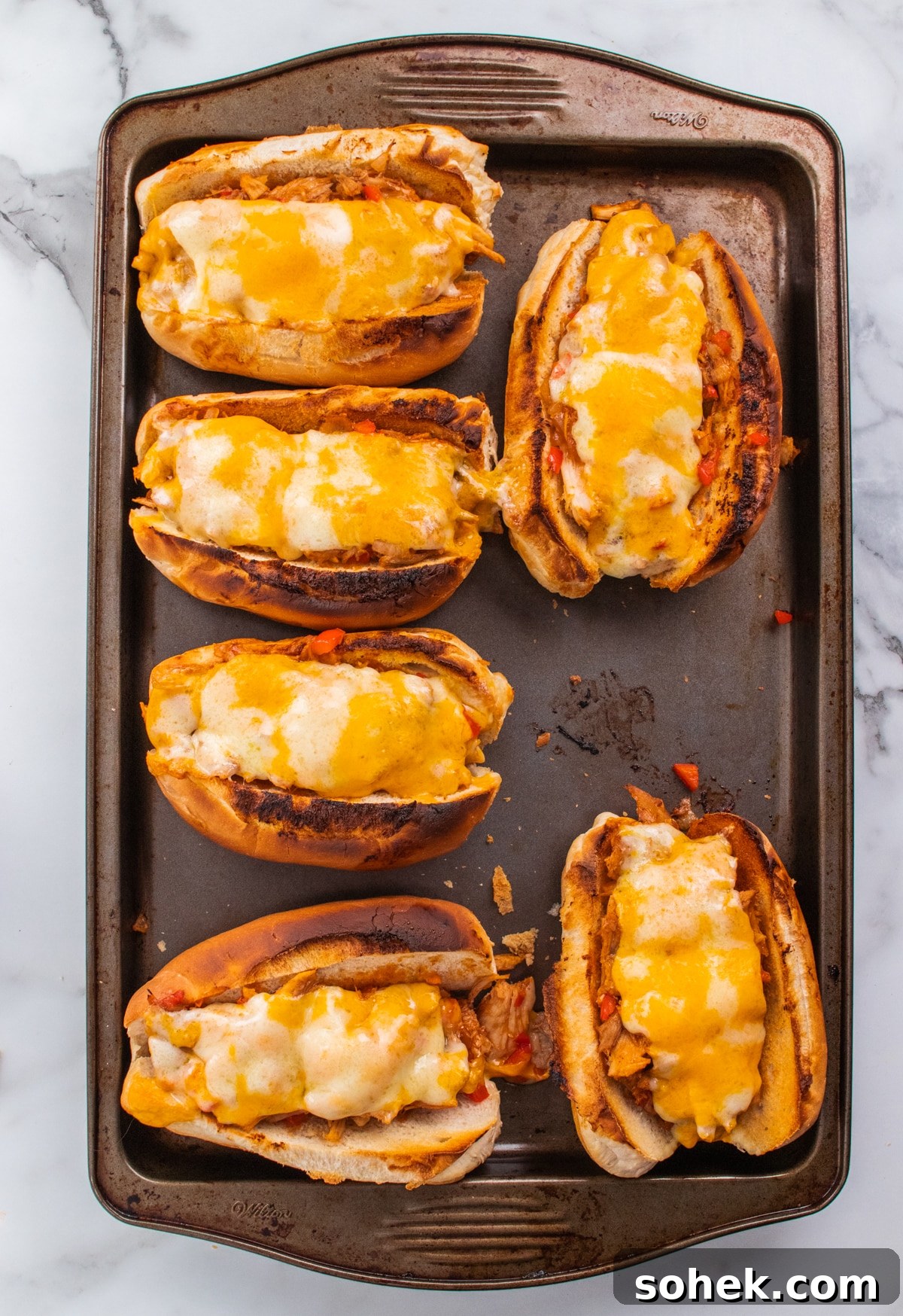 Baking sheet filled with cheesy toasted leftover turkey sandwiches.