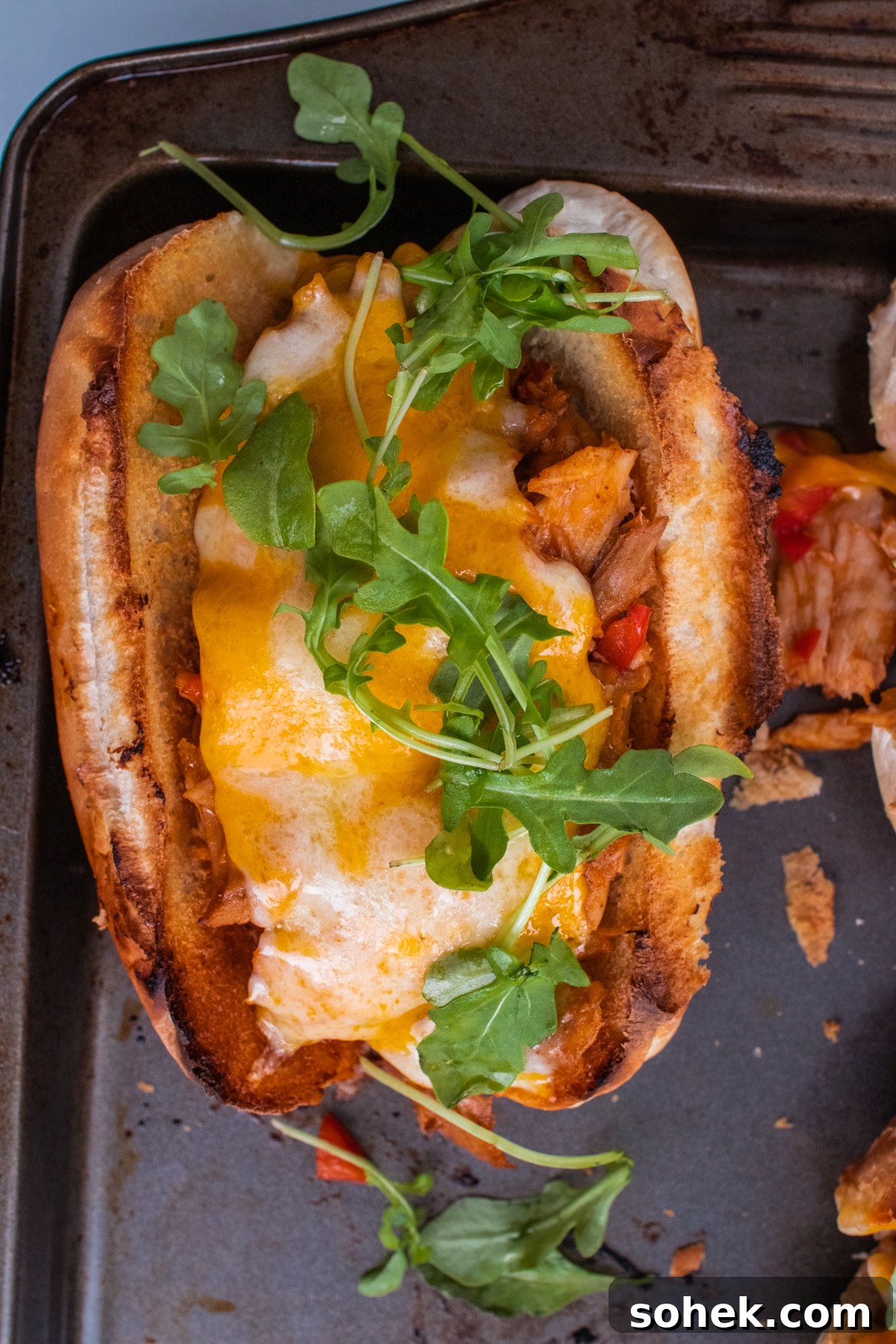 Toasted hoagie roll filled with smoked turkey, melted Colby Jack cheese, and fresh arugula on a baking sheet.