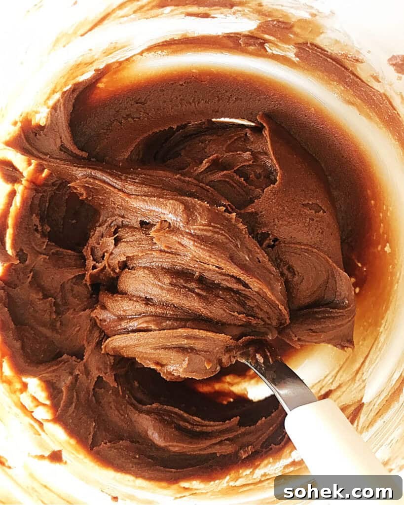 Decadent Chocolate Peanut Butter Frosting Recipe 4 Glass bowl with peanut butter chocolate frosting. White silver spoon inside. Top view.