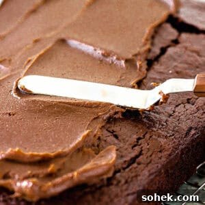 Decadent Chocolate Peanut Butter Frosting Recipe 7 Offset spatula spreading chocolate and peanut butter frosting on a rectangular chocolate cake.