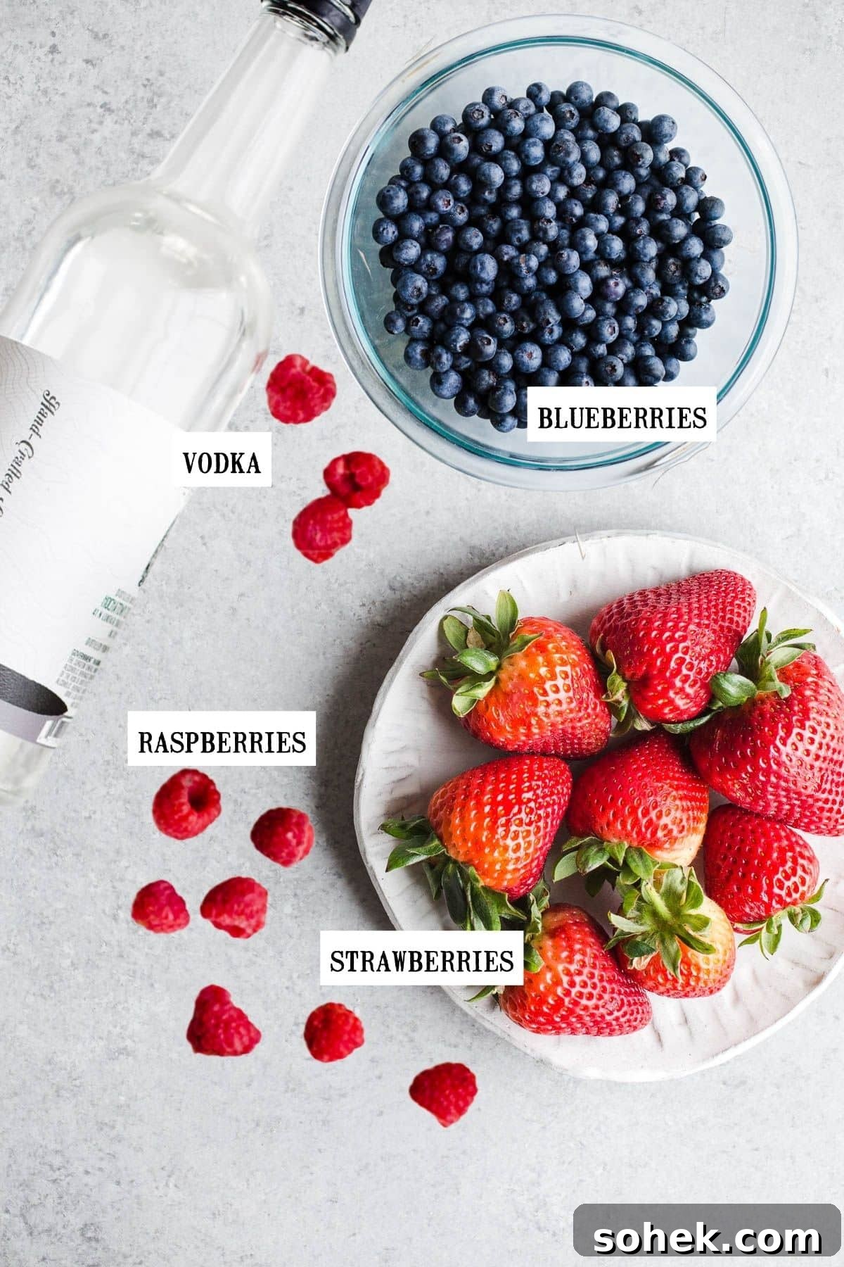 Berries and a bottle of liquor on a gray surface.
