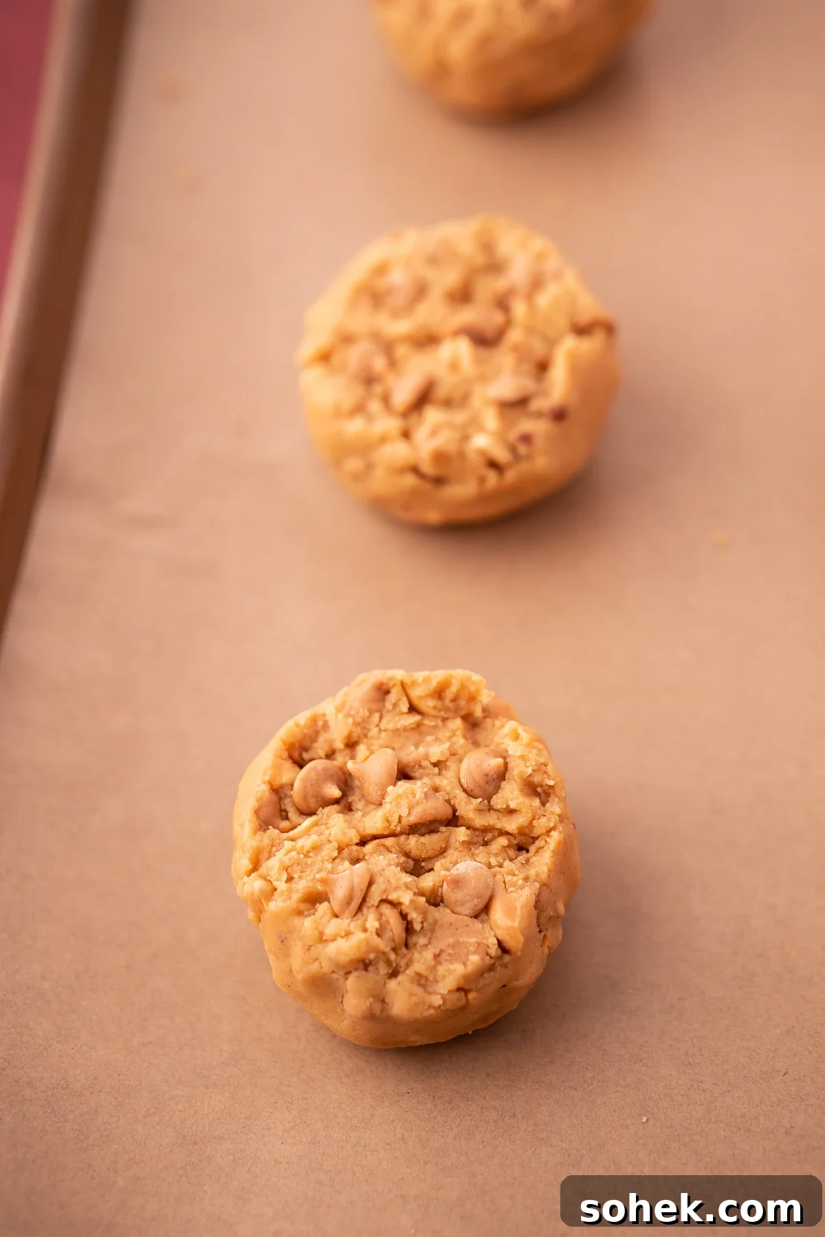 Bakery-Style Peanut Butter Cookies Recipe 6 Triple Peanut Butter Cookie Dough balls on a baking sheet lined with parchment paper.