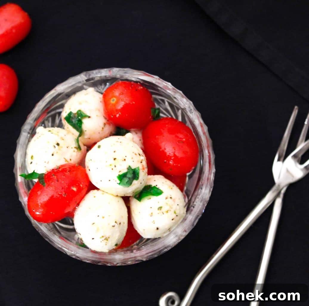 Classic Caprese Salad Recipe with Fresh Mozzarella & Basil 3 Grape tomatoes and mozzarella balls in a glass bowl with basil.
