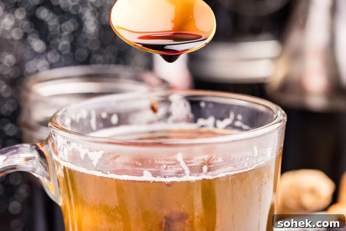 spoonful of elderberry syrup being poured into a cup of tea.