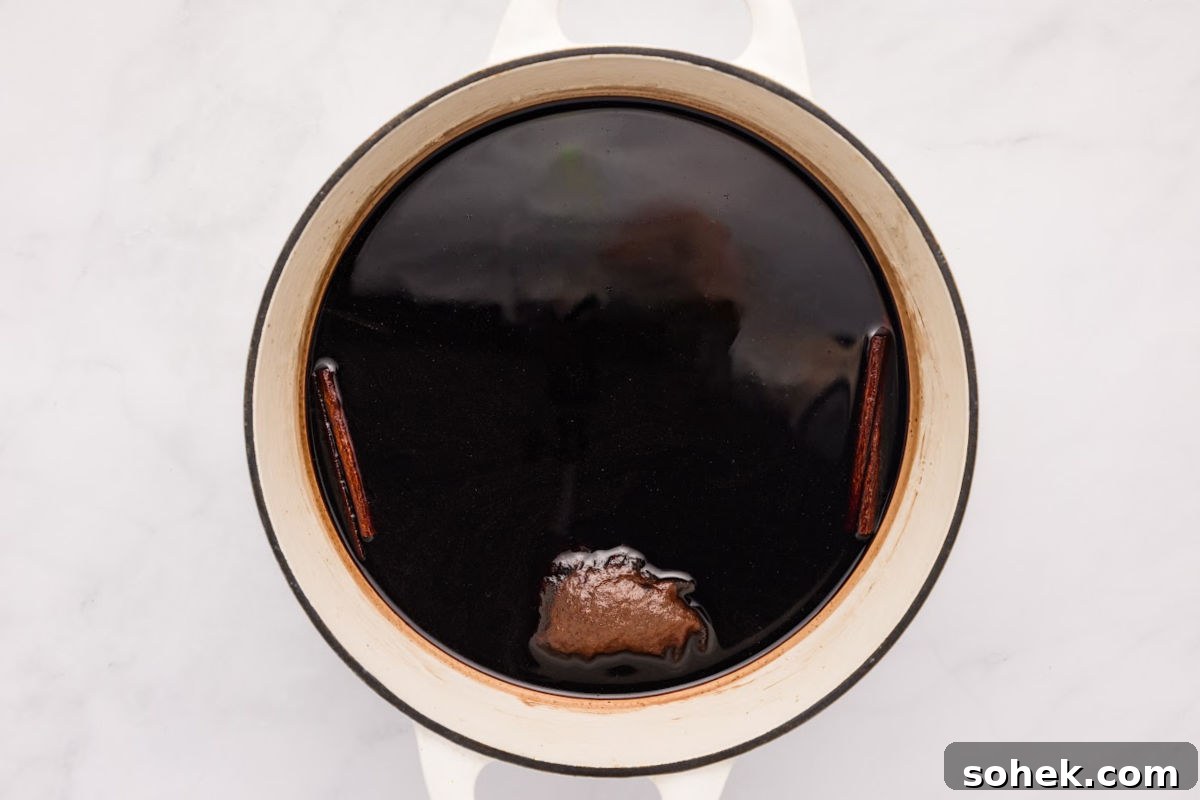 cinnamon sticks and tea bag of cloves floating on top of mixture.