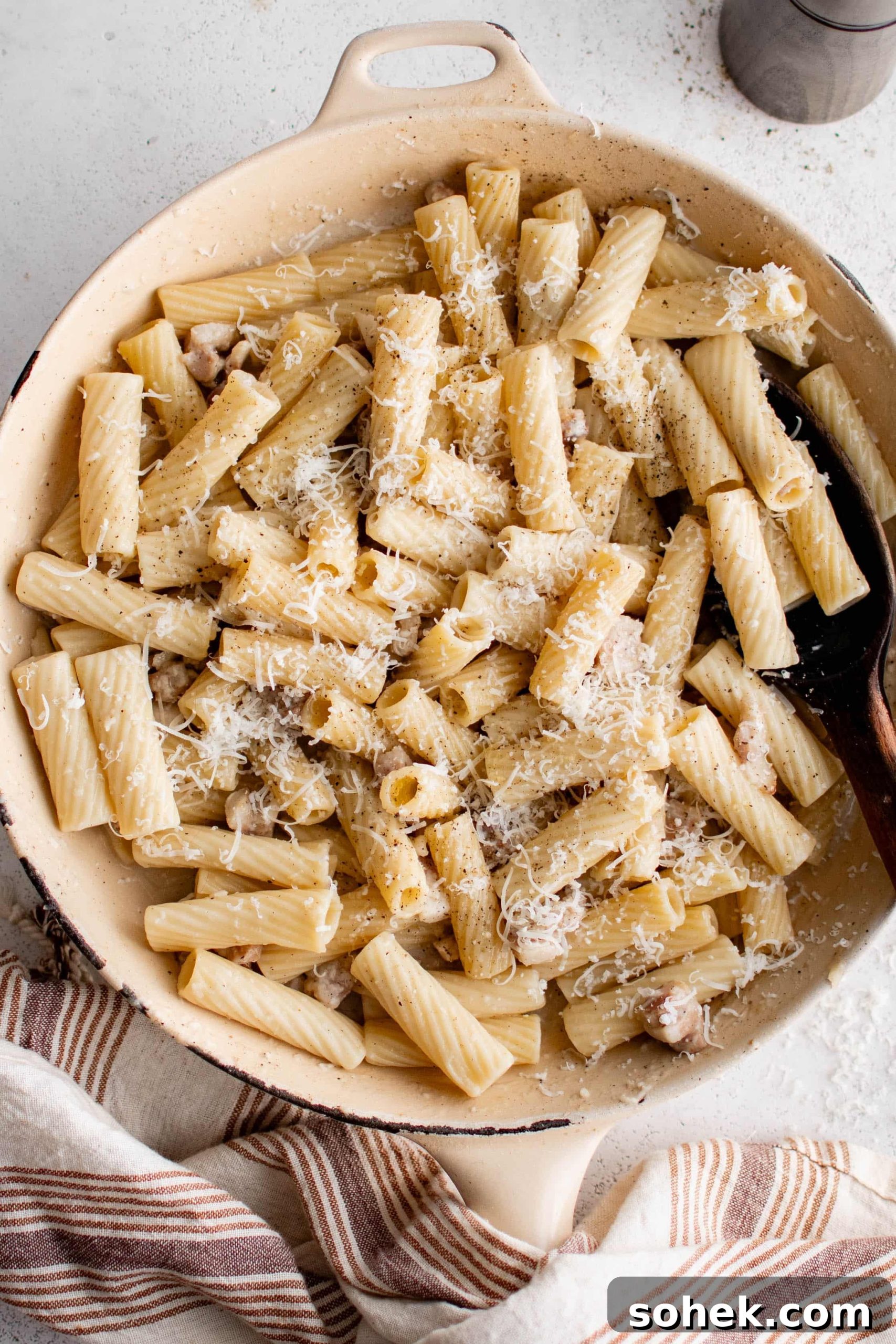 Large pan filled with Pasta Alla Gricia and sprinkled with fresh Pecorino Romano Cheese.