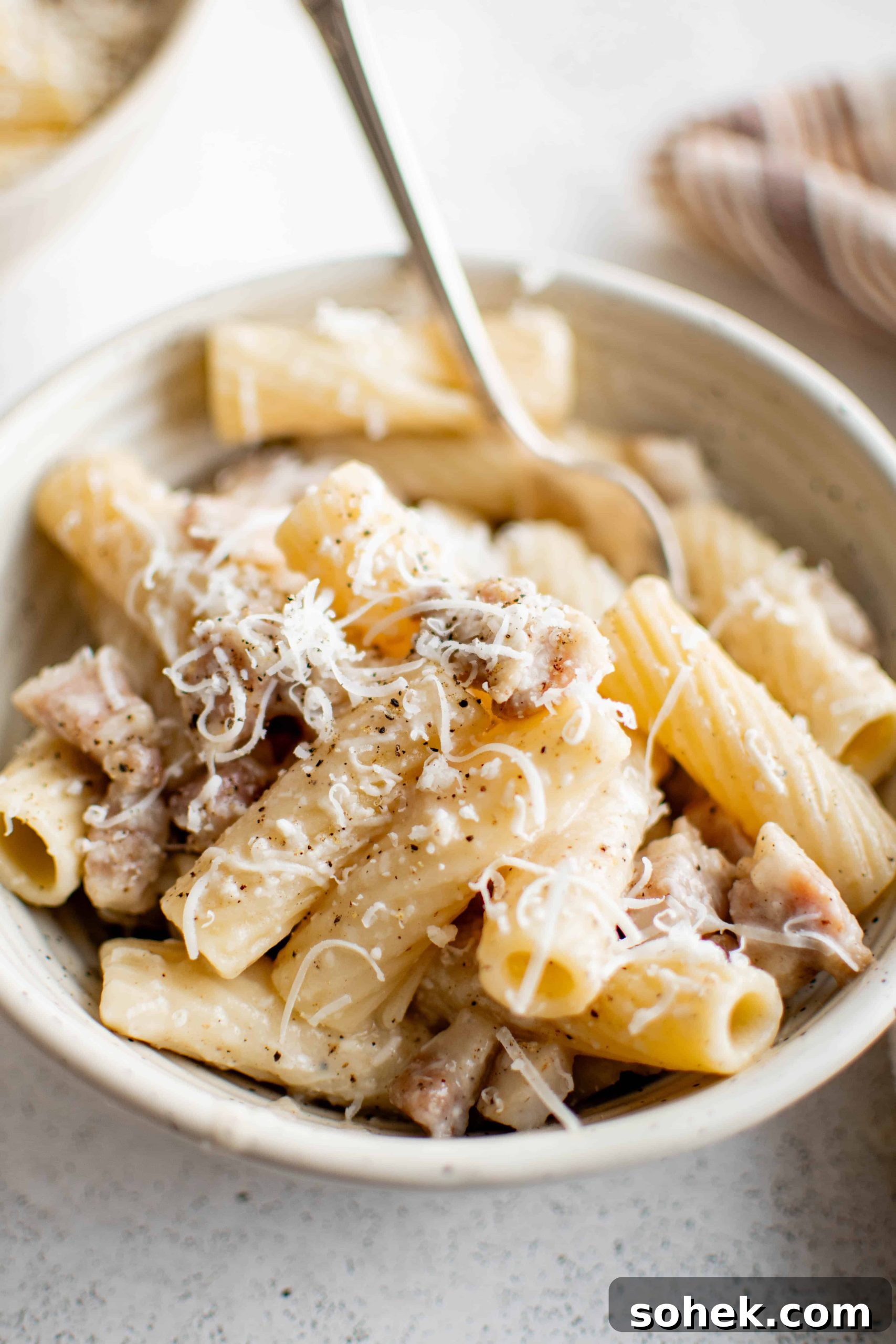 White pasta bowl filled with rigatoni alla gricia with guanciale and garnished with shredded pecorino romano cheese.