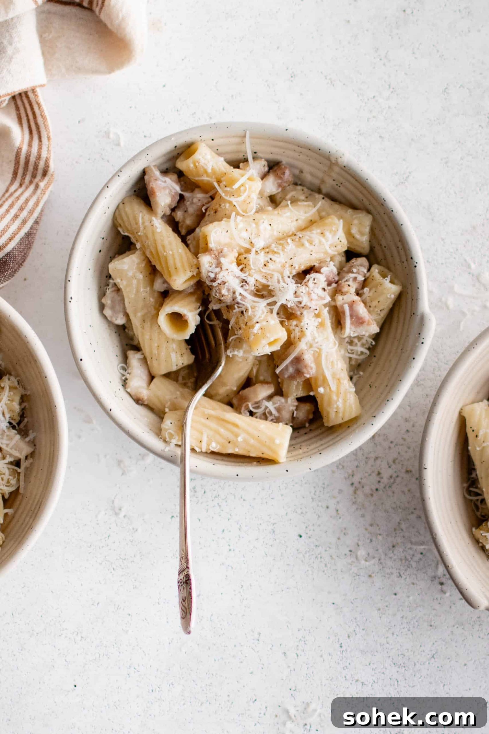 Multiple bowls filled with  rigatoni alla gricia with guanciale and garnished with shredded pecorino romano cheese.
