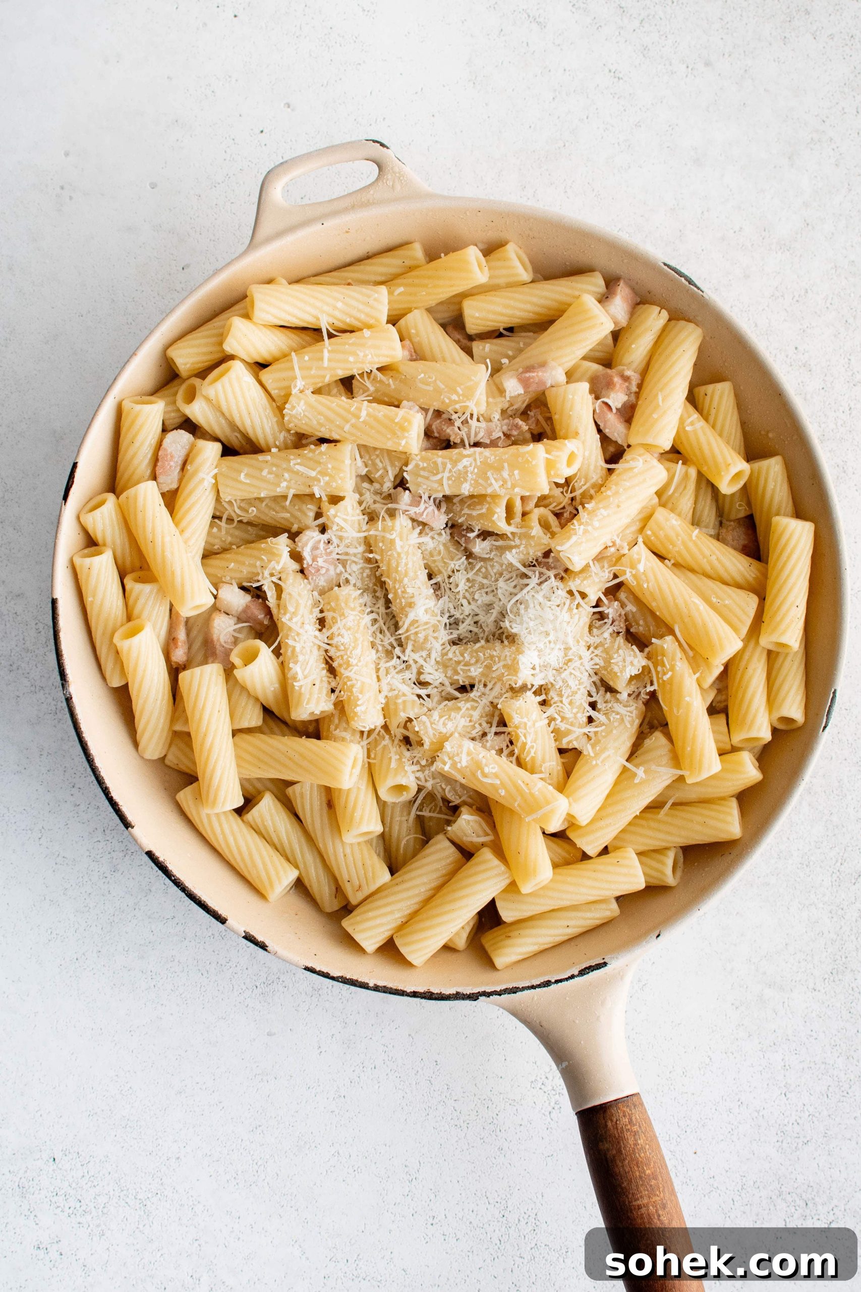 Large pan filled with al dente rigatoni mixed together with cooked guanciale and pasta cooking water mixed with rendered pork fat and topped with grated pecorino romano cheese.