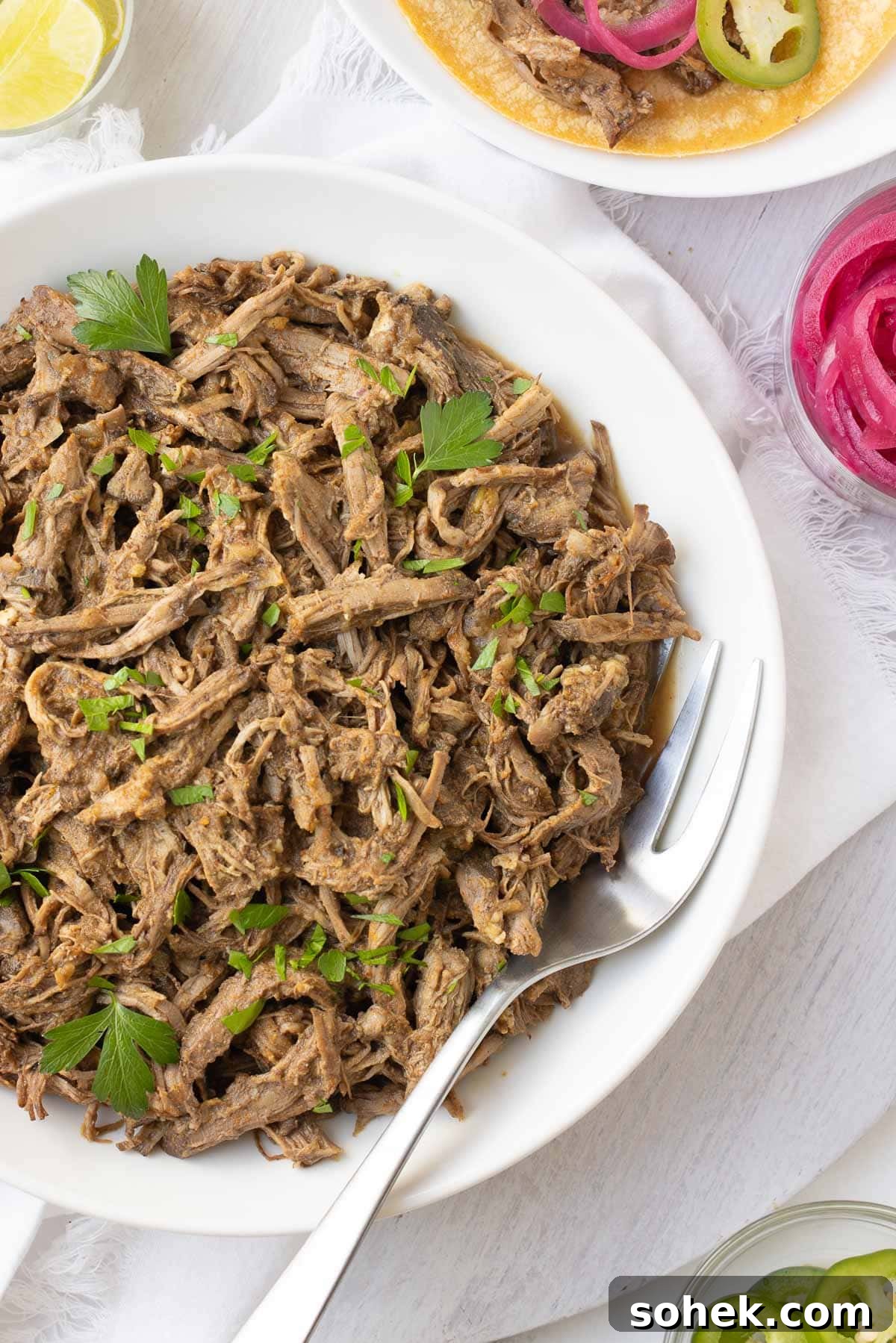 Slow Cooker Shredded Beef Recipe for Sandwiches and Tacos 2 A bowl of juicy brown shredded beef made in a slow cooker with herbs and pink pickled onions.