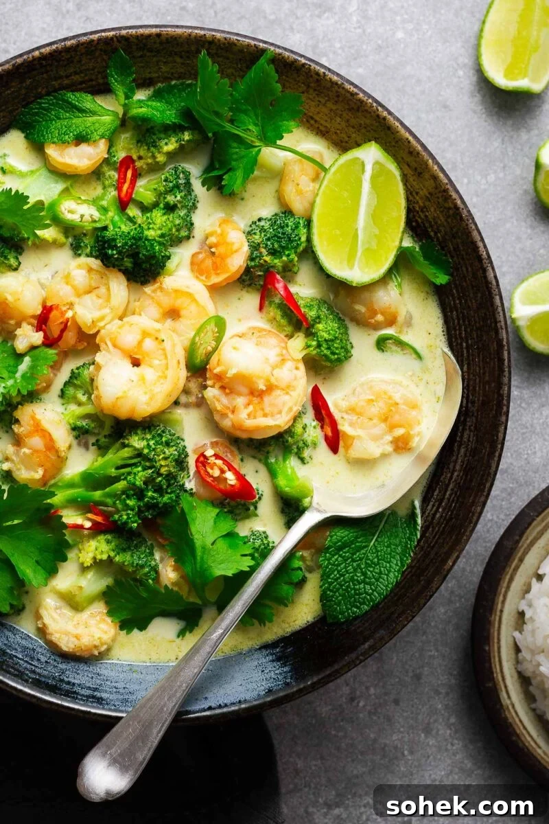 Spicy Thai Green Mango Salad (Yam Ma Muang) — Tangy Mango Thai Salad 13 A ceramic bowl with Thai green curry with shrimp and broccoli garnished with fresh herbs and lime wedges with a serving spoon.