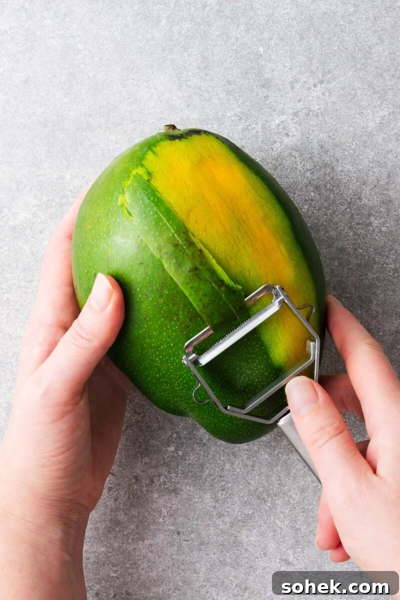 Spicy Thai Green Mango Salad (Yam Ma Muang) — Tangy Mango Thai Salad 6 Two hands peeling a green mango with a vegetable peeler.