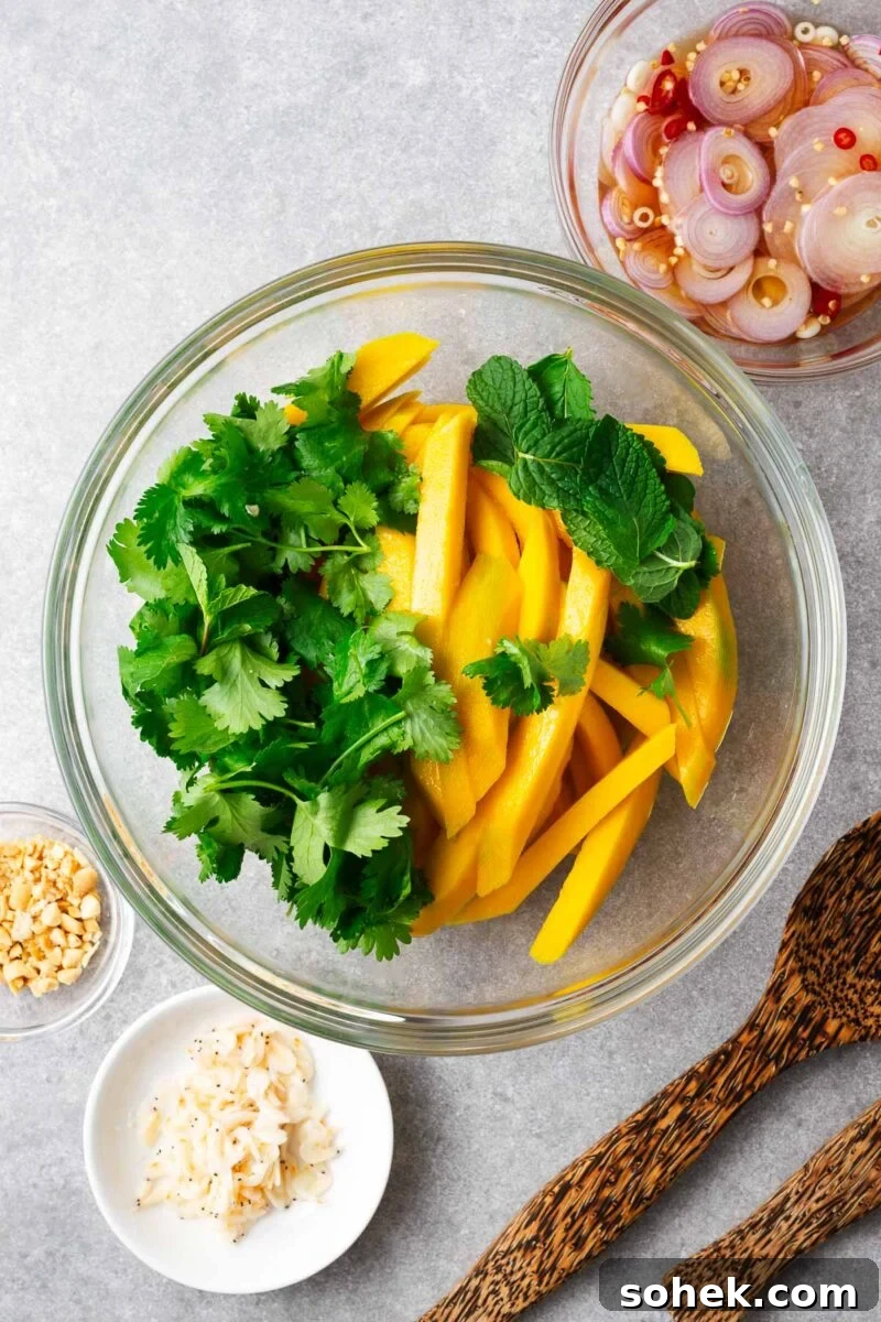 Spicy Thai Green Mango Salad (Yam Ma Muang) — Tangy Mango Thai Salad 7 A large mixing bowl with thinly sliced green mango strips and fresh herbs.