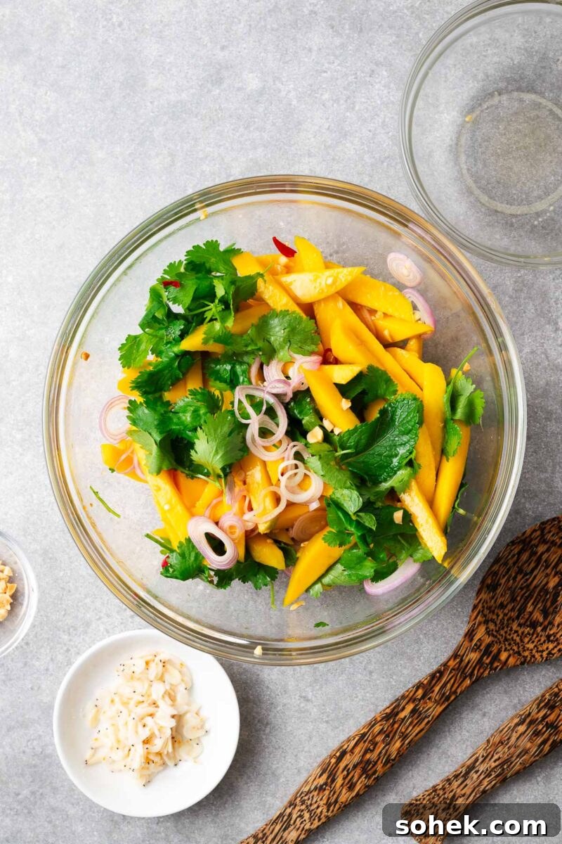 Spicy Thai Green Mango Salad (Yam Ma Muang) — Tangy Mango Thai Salad 8 Assembling the Thai mango salad in a large glass bowl with the salad ingredients and salad dressing.