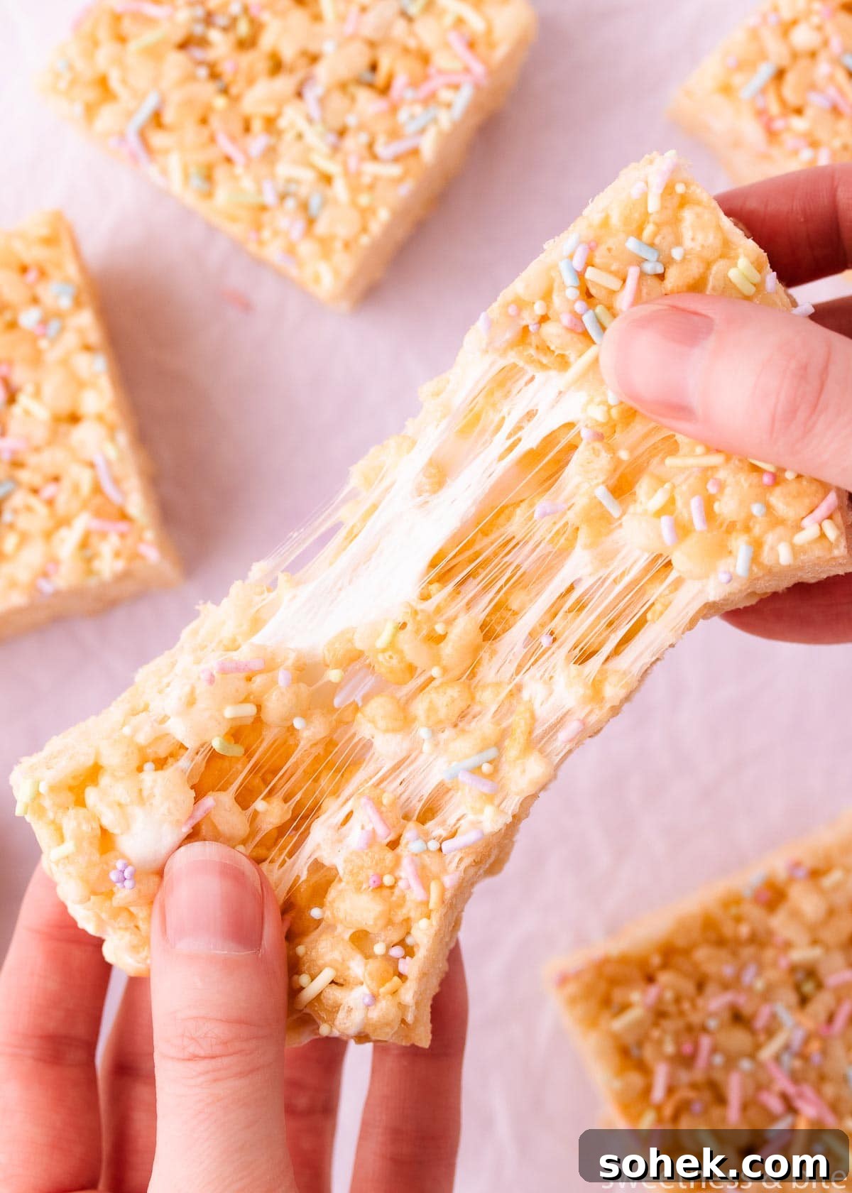 Gluten-Free Rice Krispie Treats Recipe — Crispy & Chewy Bars 3 A gluten free rice krispie treat being pulled apart by two hands, showing the marshmallow stretching as it is pulled.