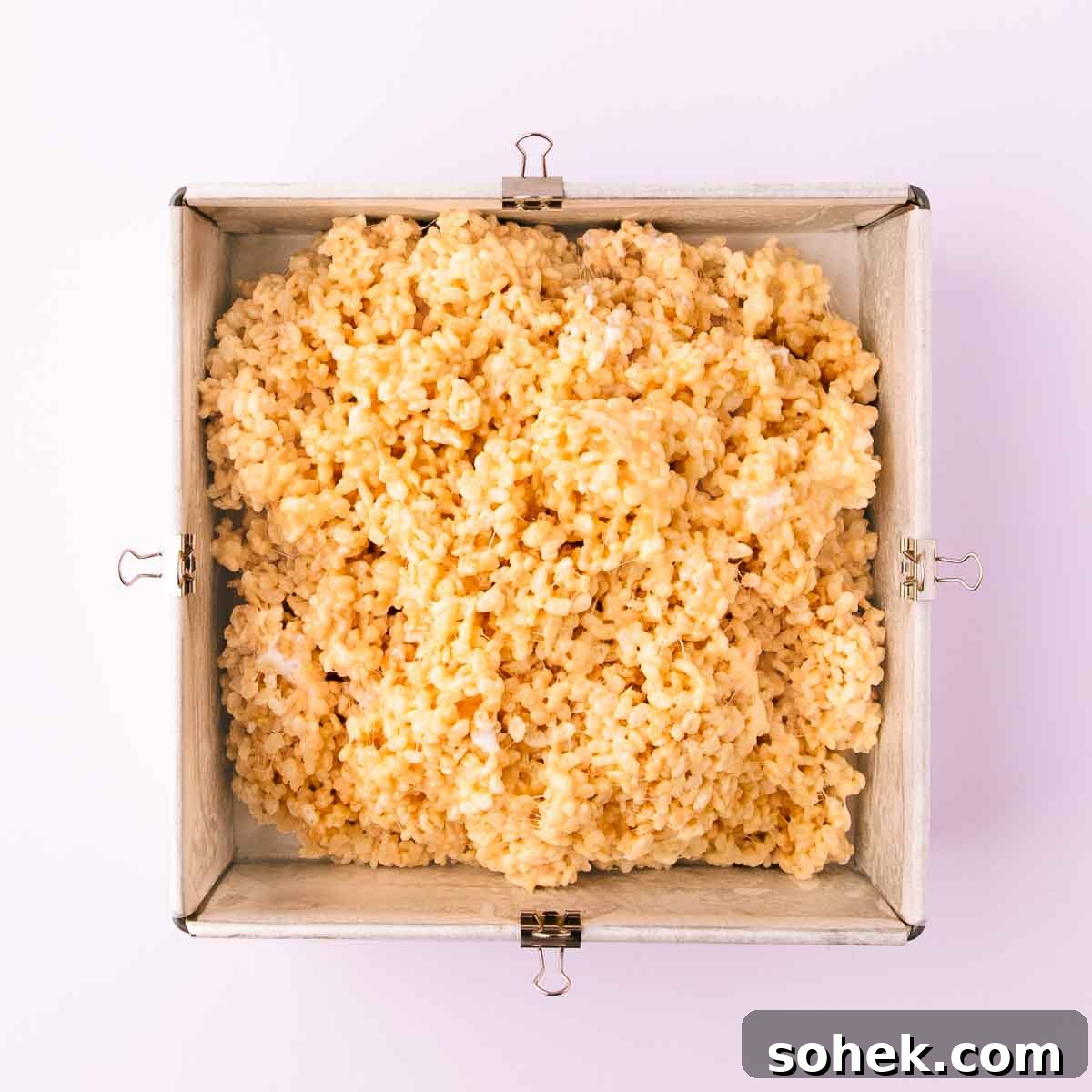 Gluten-Free Rice Krispie Treats Recipe — Crispy & Chewy Bars 9 The rice krispie mixture piled into a baking paper lined square cake pan.