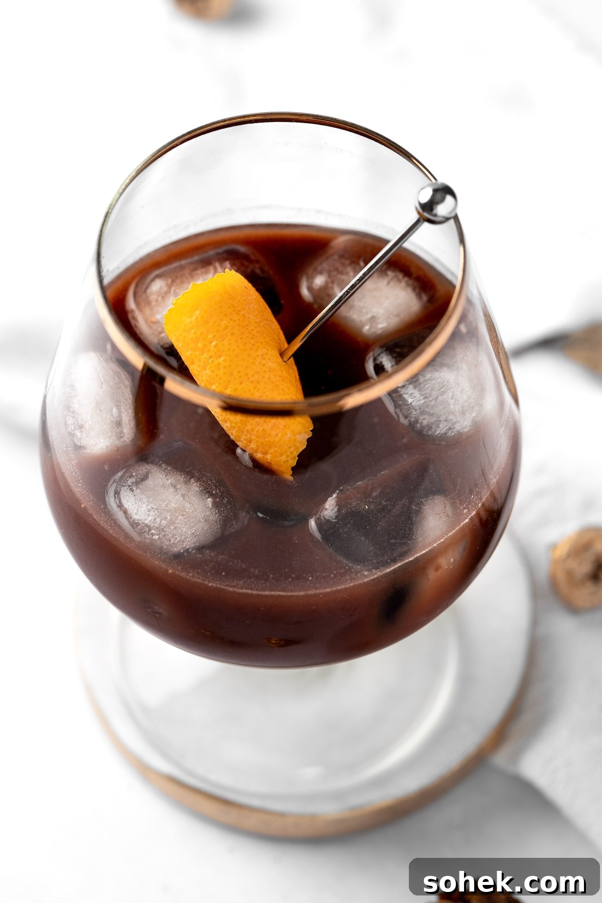 Chocolate Old Fashioned Cocktail Recipe & How to Make It 2 A chocolate old fashioned garnished with an orange peel, on a white and gold coaster.