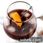A chocolate old fashioned garnished with an orange peel, on a white marble table.