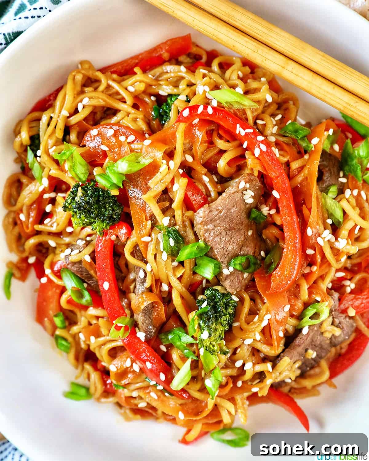 Sesame Garlic Noodles with Steak, broccoli, red peppers, carrots, in a white bowl with chopsticks.
