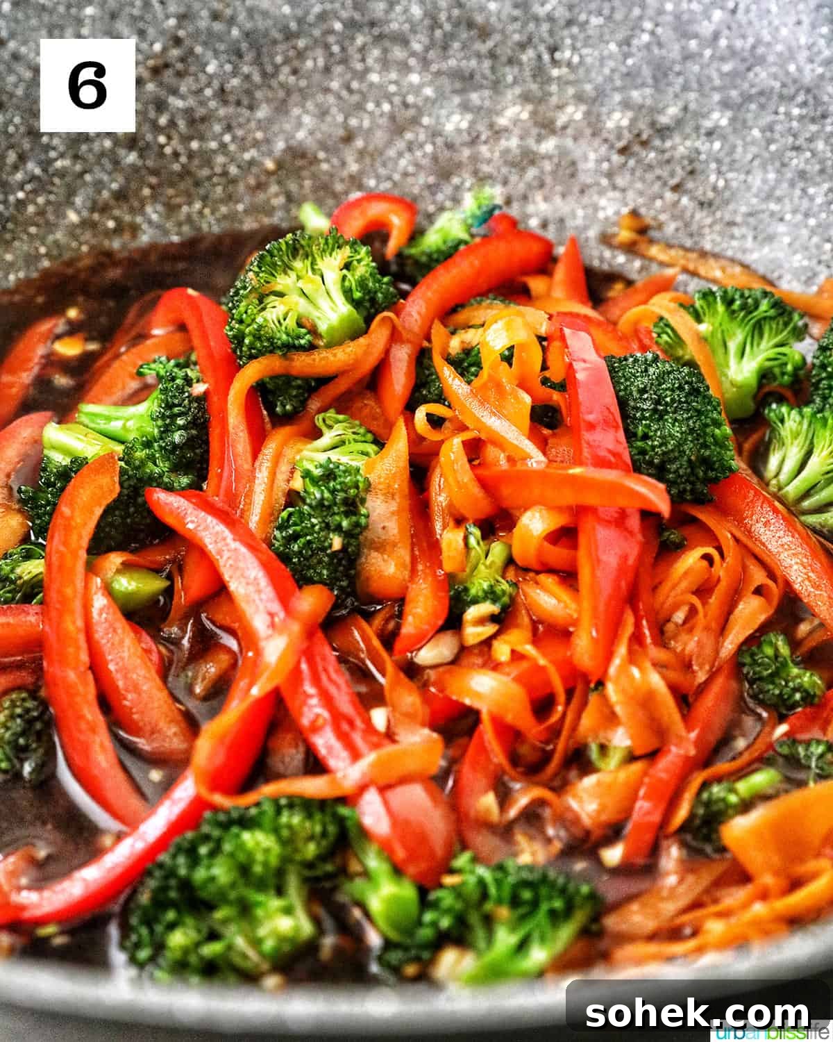 carrots, broccoli, red bell peppers stir-frying in a large wok with soy sauce.
