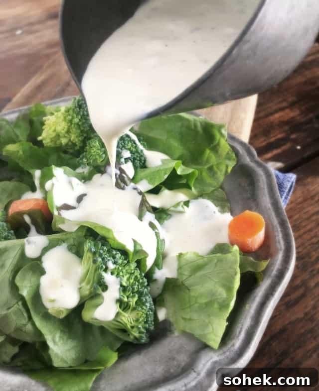Copycat Restaurant-Style Ranch Dressing Recipe for Flavorful Salads 2 Silver bowl pouring restaurant ranch dressing onto green salad on grey plate