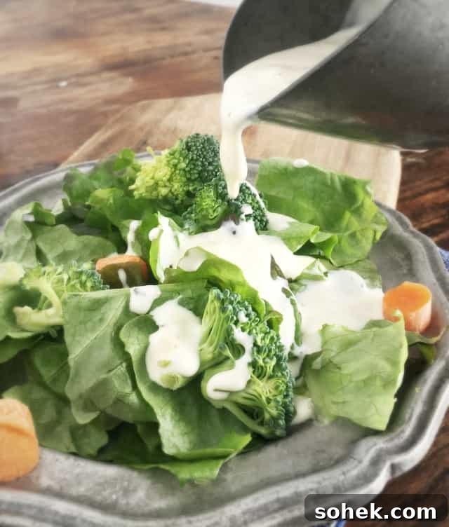 Copycat Restaurant-Style Ranch Dressing Recipe for Flavorful Salads 3 Creamy white restaurant ranch dressing pouring onto a green salad with orange carrots and green broccoli on a grey plate