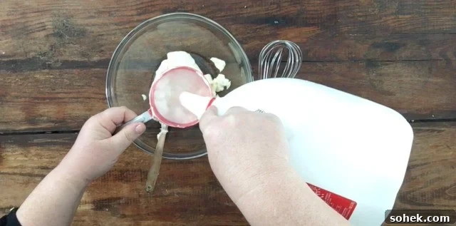 Copycat Restaurant-Style Ranch Dressing Recipe for Flavorful Salads 5 A photo of pouring milk into a cup measure for Restaurant Ranch Dressing. Large glass bowl and whisk to the right.