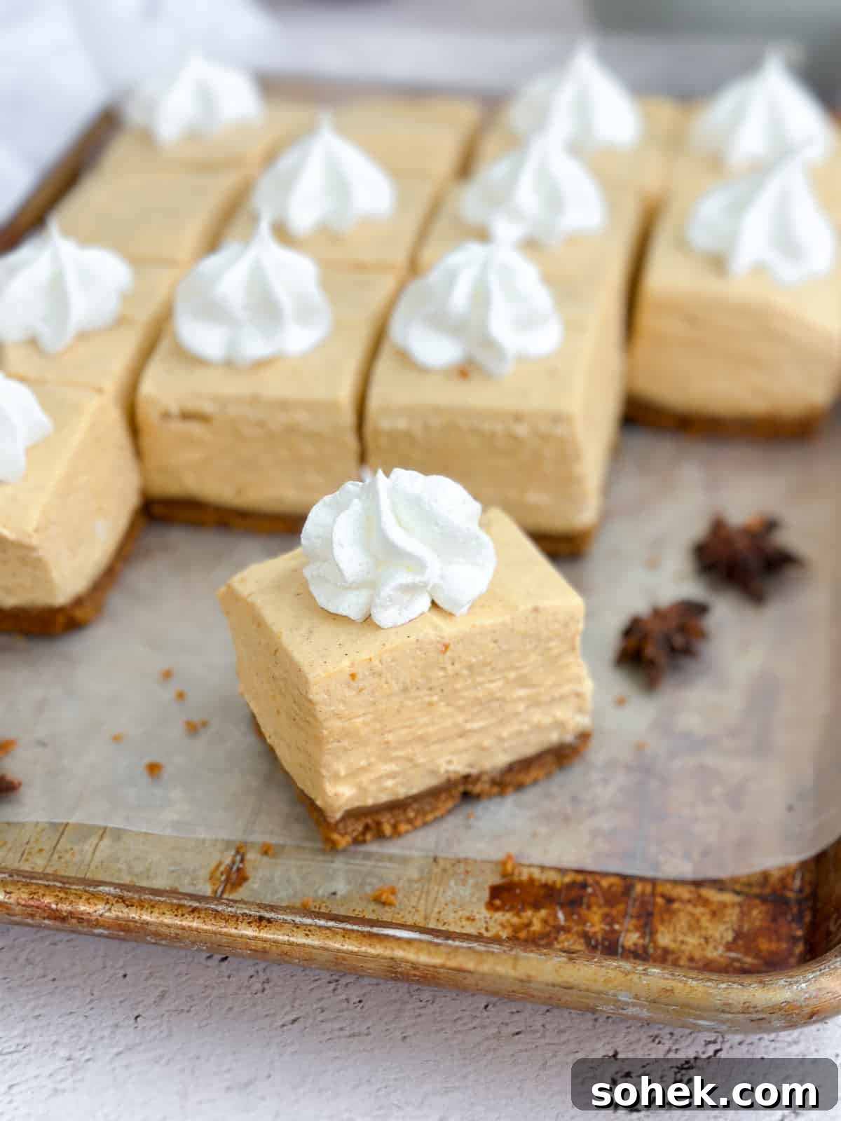 No-Bake Pumpkin Cheesecake Bars — Creamy Fall Dessert Recipe 2 a close up of a square of no bake pumpkin cheesecake bars on a baking sheet.