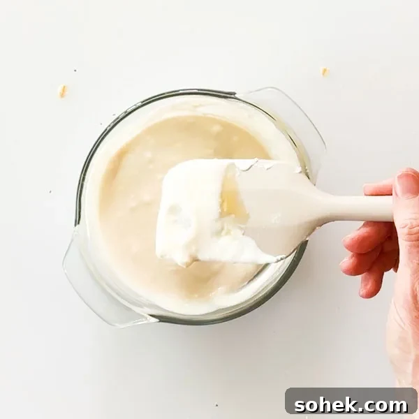 Mixed greek yogurt in a glass bowl with a spatula.