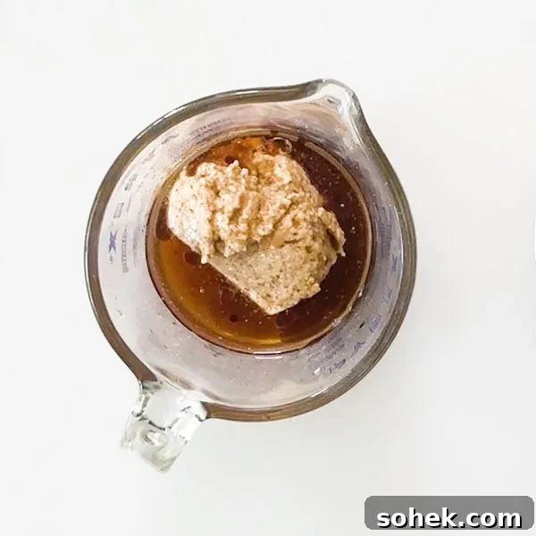 Almond butter and maple syrup in a glass measuring bowl.
