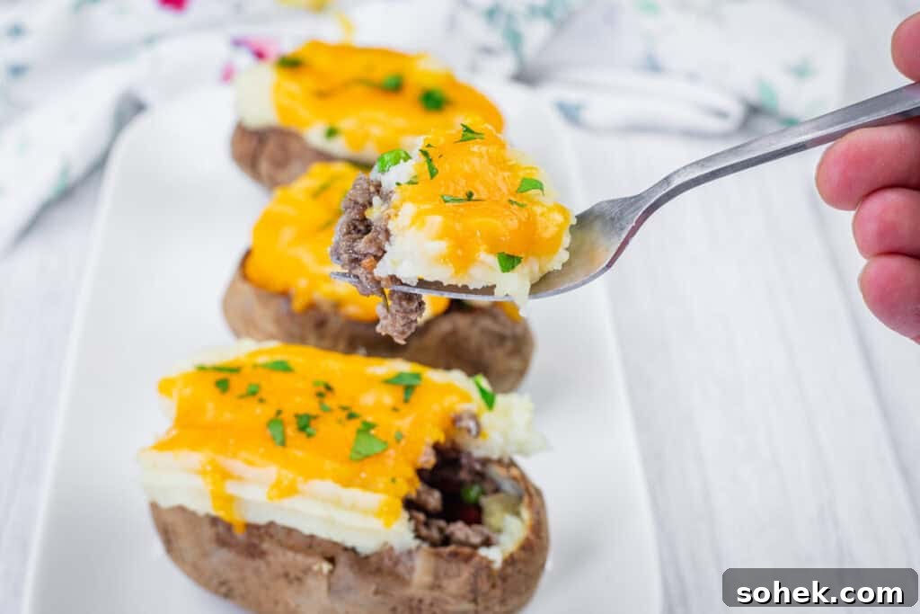 21 Quick Ground Beef Dinners That Will Have Everyone Asking Your Secret 2 A fork holds a bite of Shepherd’s Pie Stuffed Baked Potatoes on a white plate with additional loaded potatoes in the background.