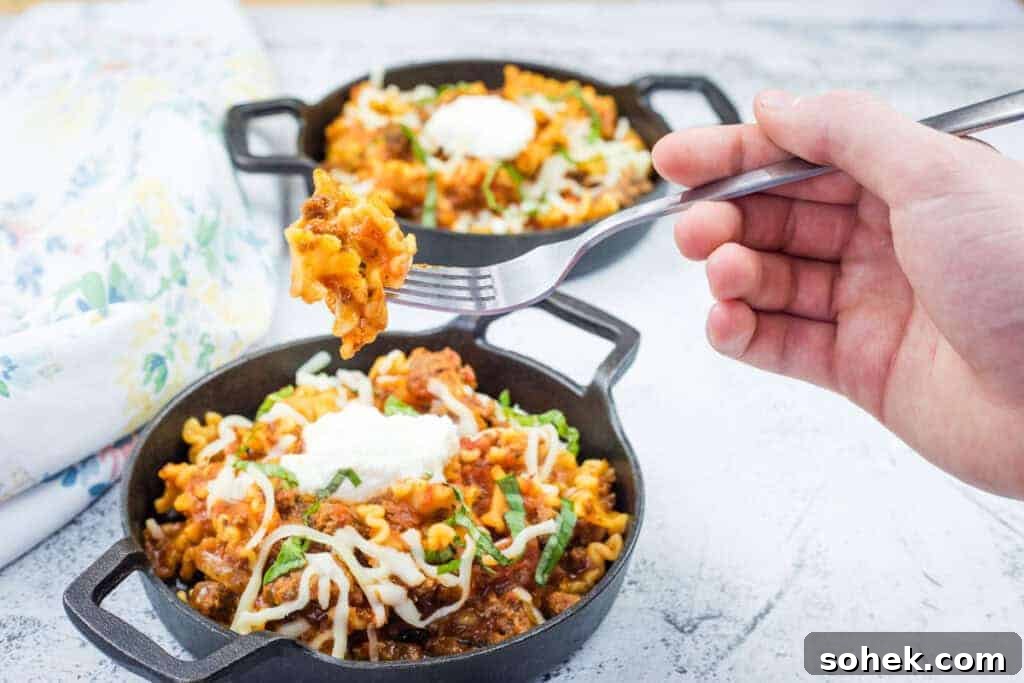 21 Quick Ground Beef Dinners That Will Have Everyone Asking Your Secret 11 A hand holds a fork with a Classic Skillet Lasagna with Ground Beef topped with melted cheese and herbs.