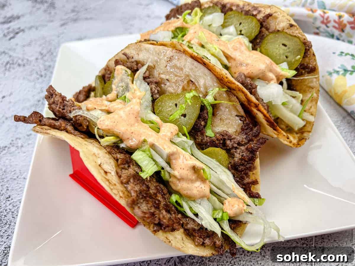 21 Quick Ground Beef Dinners That Will Have Everyone Asking Your Secret 14 Two Big Mac tacos filled with ground beef, shredded lettuce, and pickles, and drizzled with a creamy sauce, placed on a white plate.