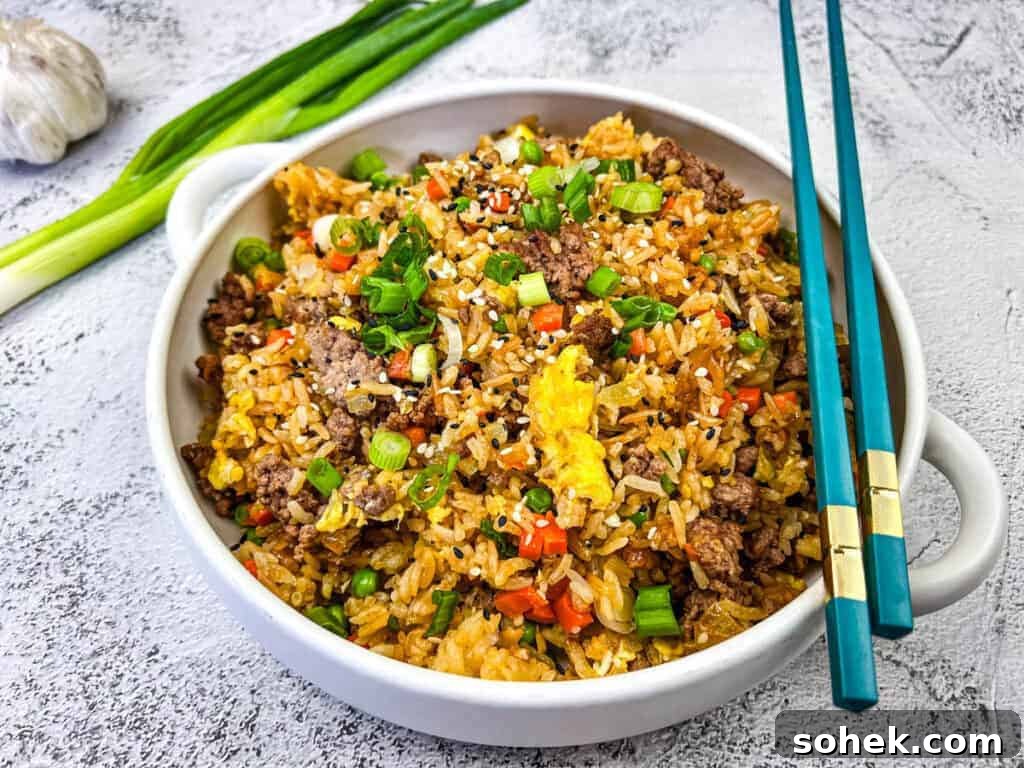 21 Quick Ground Beef Dinners That Will Have Everyone Asking Your Secret 3 Ground Beef Fried Rice served in a white bowl with blue chopstick on top.