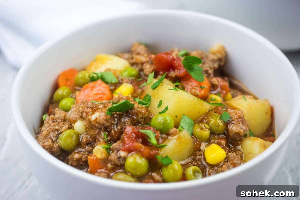 21 Quick Ground Beef Dinners That Will Have Everyone Asking Your Secret 6 A white bowl filled with easy Hamburger stew garnished with parsley.